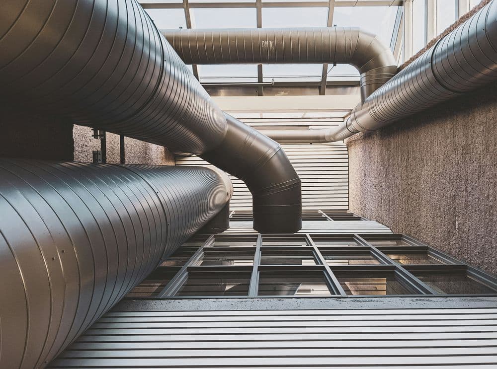Looking up at industrial piping and windows in a modern building.
