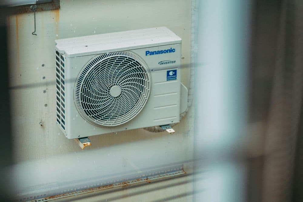 Panasonic inverter air conditioning unit mounted on a wall, viewed through a window.