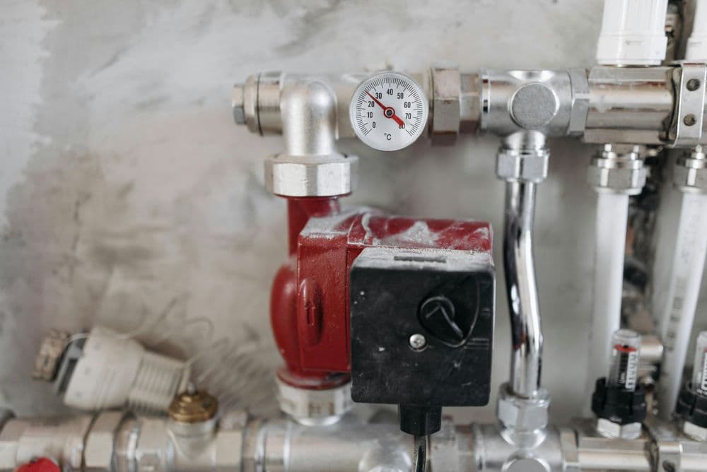 Red water pump with pressure gauge and metal piping on a gray wall.